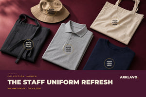 Flat lay of Arklavo custom staff apparel, a heather grey polo, charcoal apron, navy crewneck, tan bucket hat and canvas tote, each showing a Your Logo Here embroidery placement, on a mulberry background.