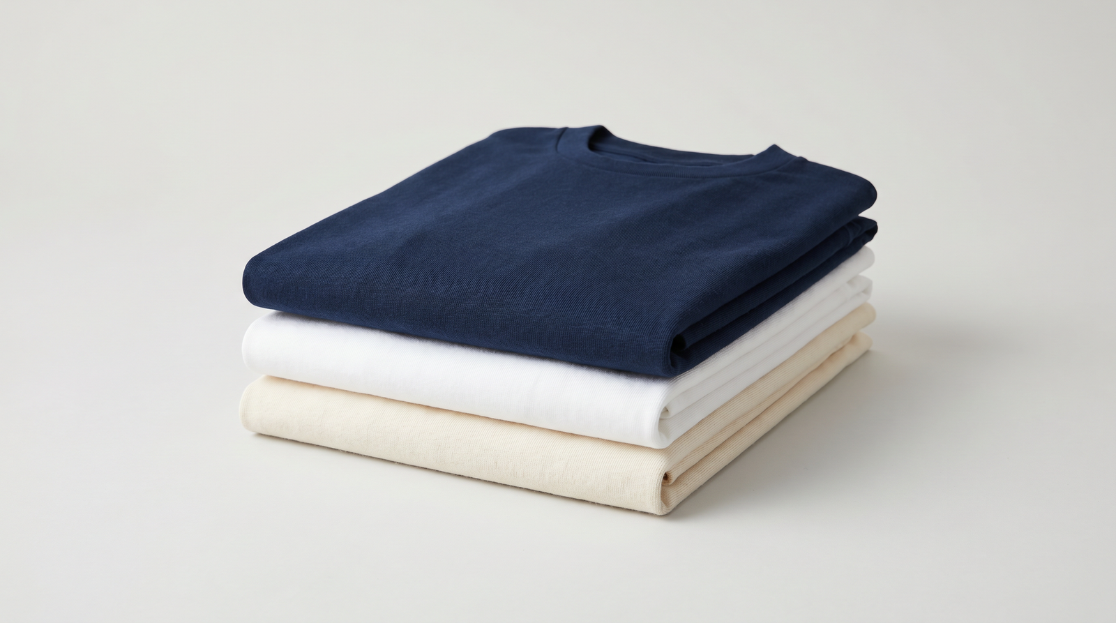Custom printed t-shirts stacked and folded - USA-made apparel from Arklavo in navy, white, and natural cotton colors