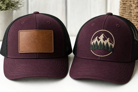 Two mulberry trucker hats side by side, one with a tan leather patch and one with a stitched thread embroidered emblem, showing the texture difference