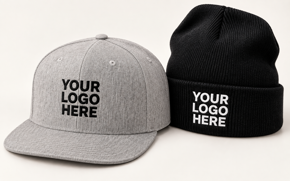 Grey snapback with black YOUR LOGO HERE embroidery beside a black beanie with white cuff embroidery.