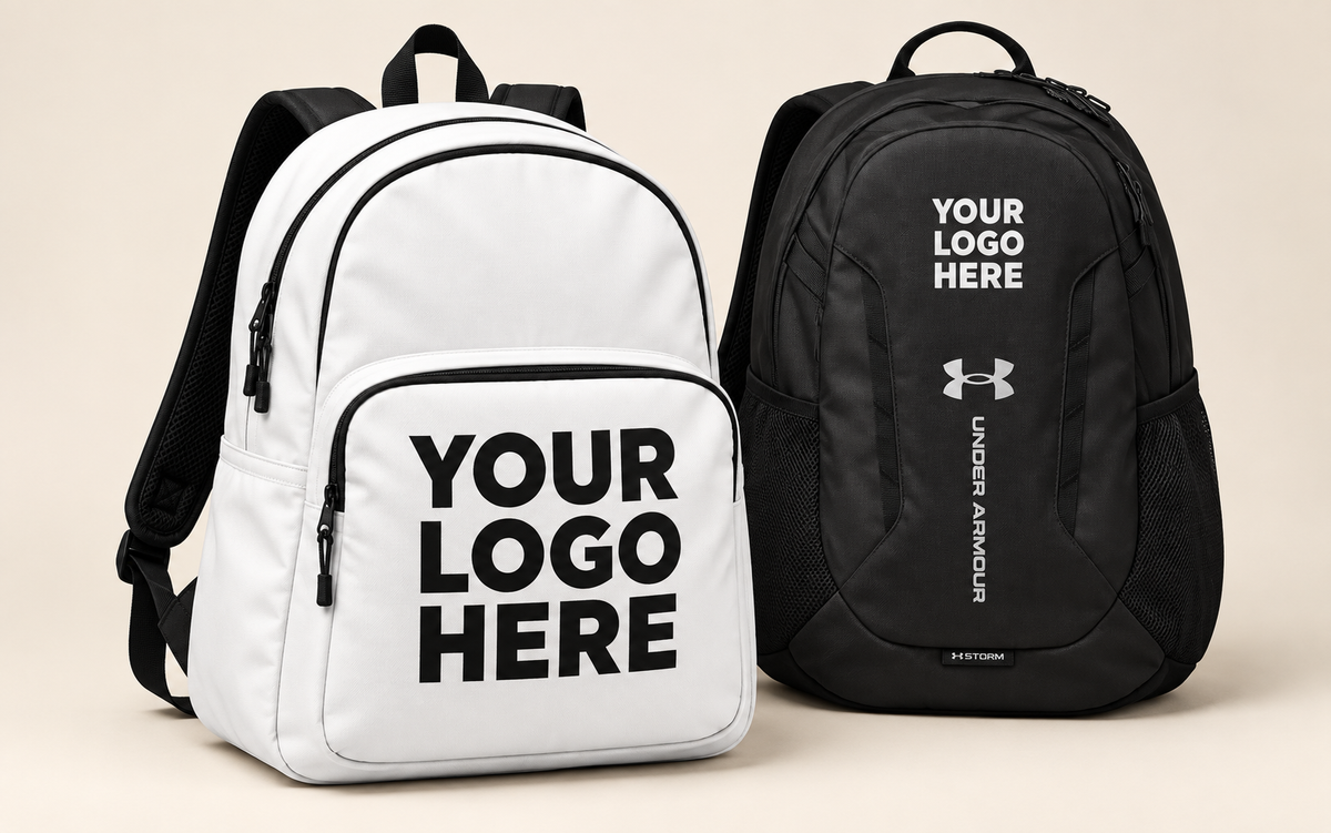 White printed backpack and black Under Armour backpack with contrasting YOUR LOGO HERE lettering clear of zips.