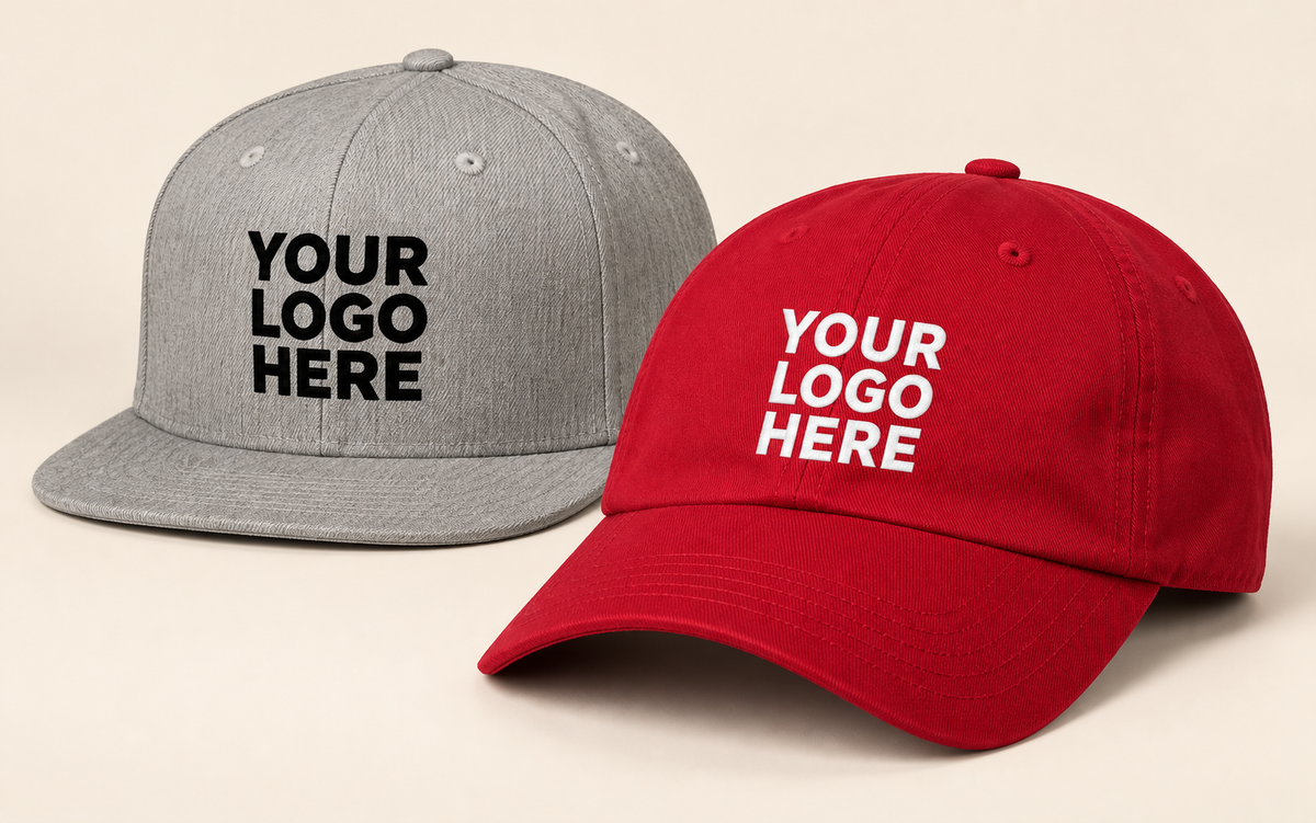 Grey flat-brim snapback and red curved-brim cap with contrasting YOUR LOGO HERE embroidery.