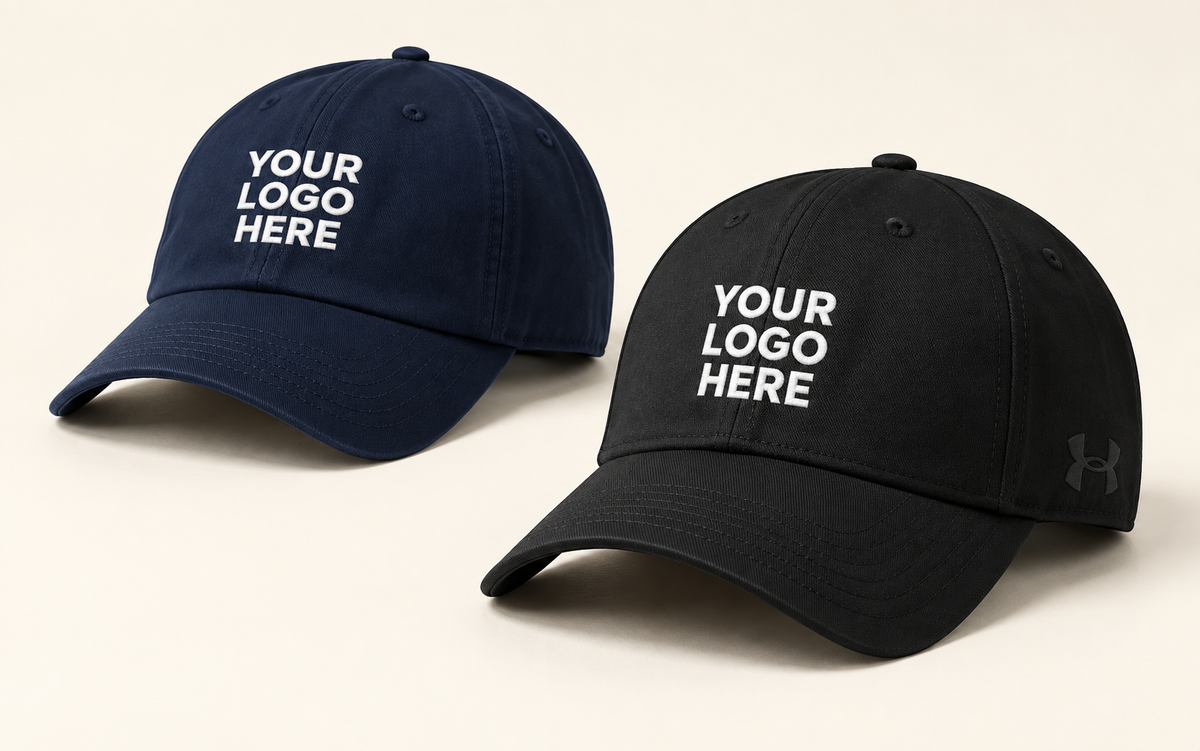 Black Under Armour cap and navy curved-brim cap with white YOUR LOGO HERE embroidery.